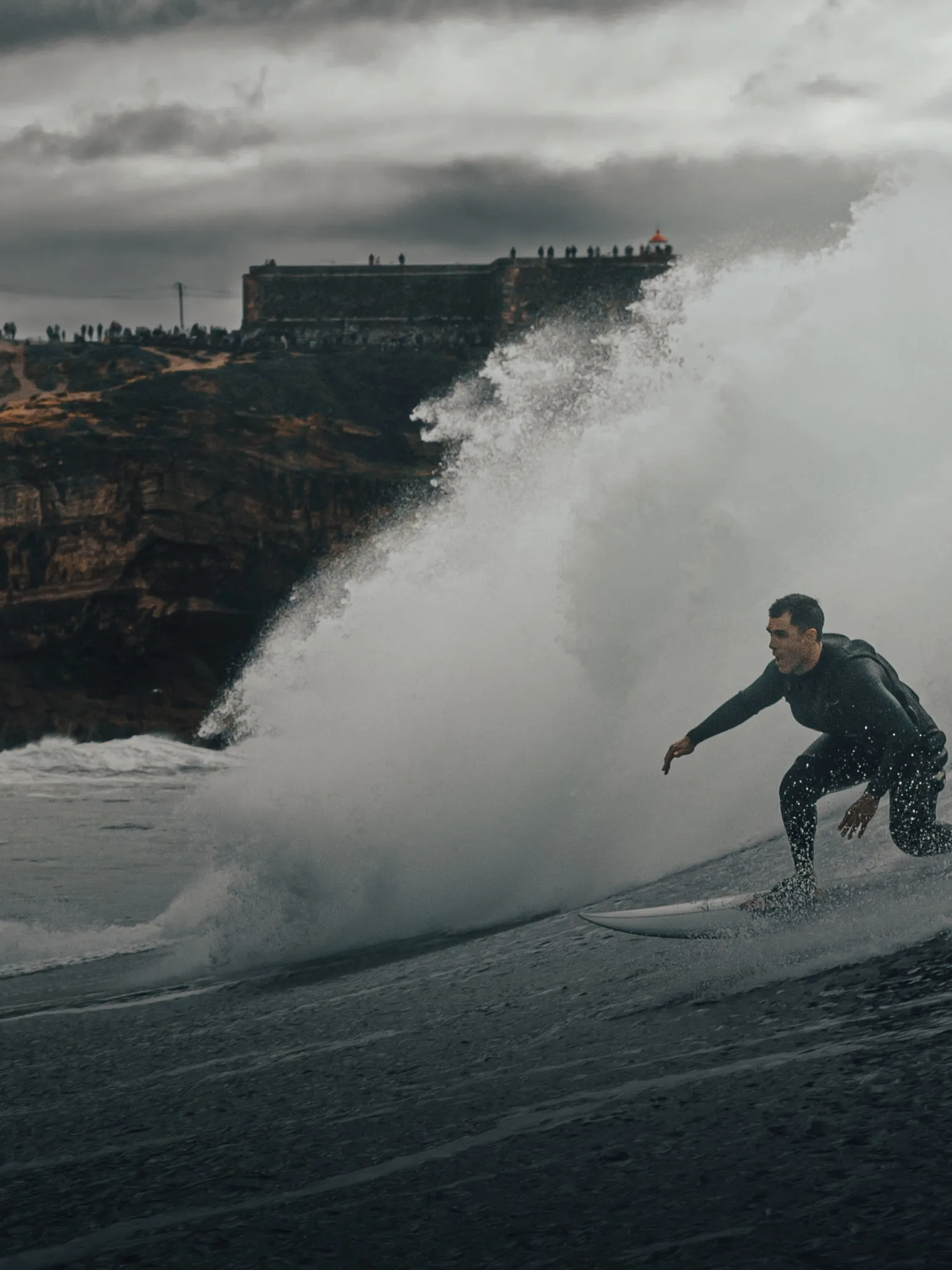 Edu riding a big wave beneath the clifftop fort at Nazare